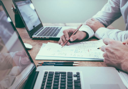person holding pencil near laptop computer